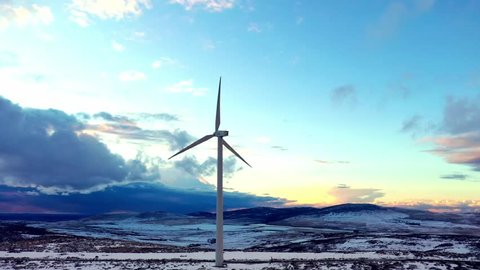 Aerial view at sunset moving along a snow covered mountain ridge with a line of wind turbines silhouetted against the evening sky, central Spain, Avila.  