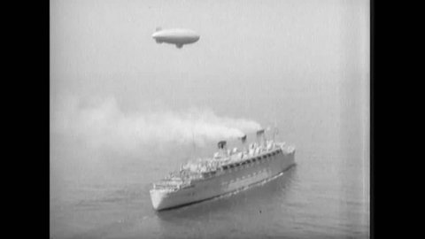 CIRCA 1930s - A nonrigid airship is flown near the RMS Queen Mary ocean liner as it travels at sea.
