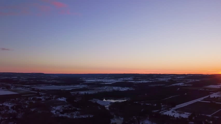 Lowering drone shot with a sunset at golden hour over a small town.