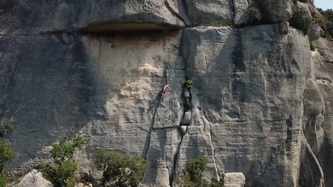 Girl epic climbing rocks in the french alps. smooth filming with the drone . Summer daylight grey and green mountain scenery around her. Trying to reach the top with power and motivation.