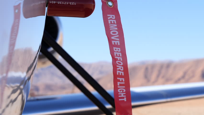 A "Remove Before Flight" tag attached to an aircraft slowly blowing in the wind, high mountains in soft focus SLOMO.
