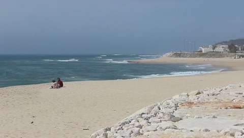 Figueira da Foz, Portugal, March 31, 2019: Family with child sitting in the distance in the sand on the beach and relaxtion on a sunny day
