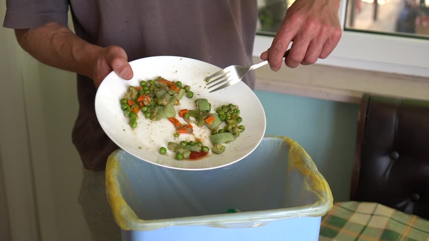 Food Loss and Waste. A man throws the uneaten food from a plate in the trash bin. Throwing away meal | Shutterstock HD Video #1027281050