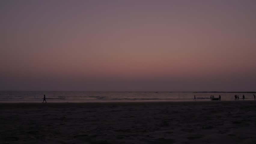 Time lapse of fisherman collecting and wrapping their fishing nets and leave exit frame against the brilliant lit sky at dusk across a vast beach while others play, walk and stroll, speed 2x