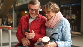 Mature gray-bearded man shows his wife a photo from his smartphone. Both have fun laughing and discussing it. Happy family travel, train station - Powered by Shutterstock - Get 15% off with code: PIKWIZARD15