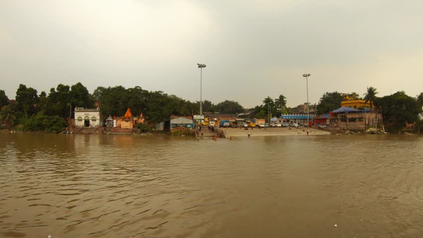 ghat indian stairs to river Hoogli people launder clothes wash themselves green trees and palms on bank view from floating boat Kolkata cloudy day