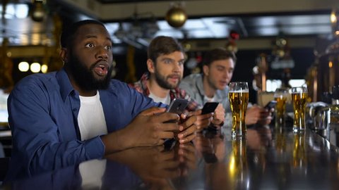 Men in bar celebrating successful bet on sports, using online bookmaker on phone