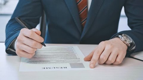 cropped view of man filling and signing document with resume lettering in office