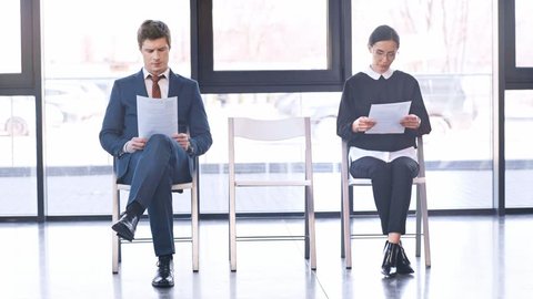 attractive woman walking in heels, sitting on chair and talking with cheerful people holding resumes before job interview