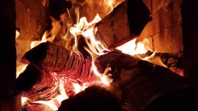Closeup of burning firewood in the fireplace against the background of red bricks. Bright fire creates flames and shadow glare along the walls. Forms bright red coals. The feeling of comfort.