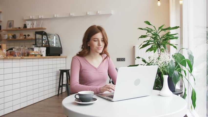 Beautiful young redhead woman working with laptop in cafe and drinking coffee | Shutterstock HD Video #1027309121