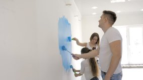 Young family paints wall with a roller while mother checking a text message