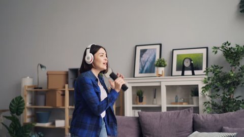 Carefree female student is enjoying music in wireless headphones dancing at home singing in remote control having fun alone. Apartment and happiness concept.