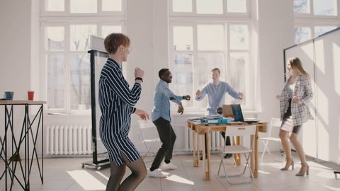 Young happy female office worker dancing together with multiethnic colleagues at fun corporate party slow motion.