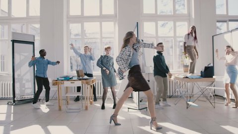 Young happy Caucasian female boss dancing in modern office celebrating together with multiethnic colleagues slow motion.