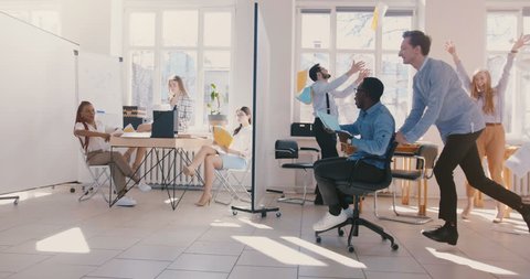 Slow motion fun young crazy African American businessman riding office chair, celebrating victory with multiethnic team. 庫存影片
