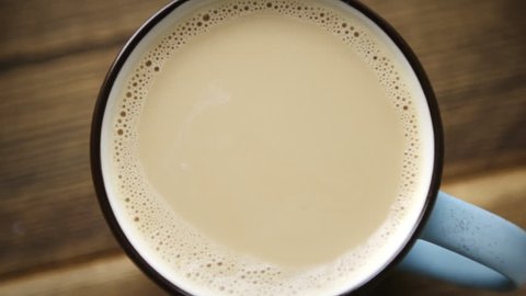 The view from the top of the slow drop of milk falls into full cup of coffee