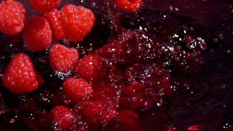 Red juicyraspberries fall into juice with beautiful splashes in slow motion