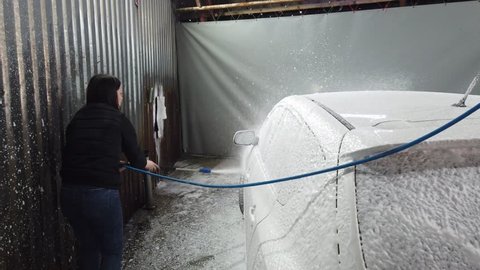 Russia, Moscow, April 2019: Brunette girl uses spray tool and covers car by froth in car-wash box.