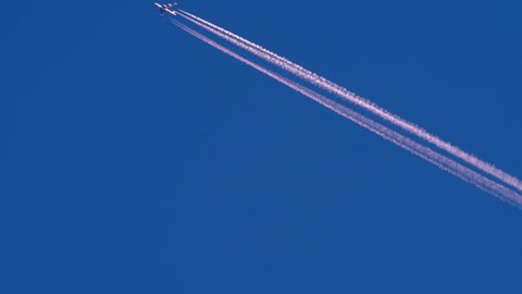 Airliner Flying High On Blue Cloudless Sky Leaving Contrails From Its Jet Engines In Atmosphere