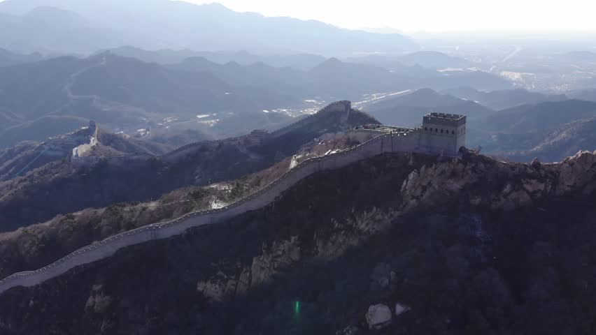 Watchtower on top point of rocky mountain, stone battlement run down on side. Aerial view of Great Wall of China at Badaling. Mountainous landscape in light mist on background