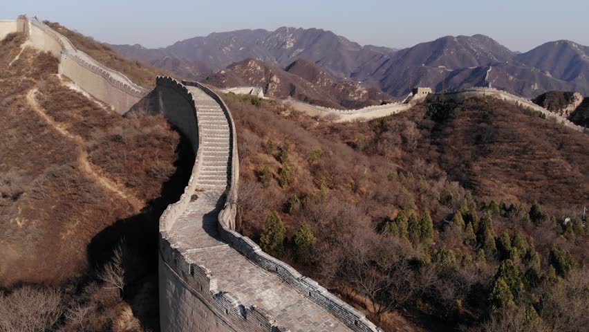 Aerial camera fly along Great Wall of China, stone fortification run up at hill side, watchtower seen on summit. Scenic shot of Badaling site