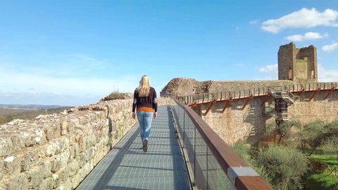 Siena, Italy: Blonde girl walks on defensive Walls of medieval village of Monteriggioni in Tuscany; architecturally significant, referenced in Dante Alighieri's Divine Comedy