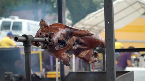 Wide shot of a pig turning on a spit over a barbecue at a festival.