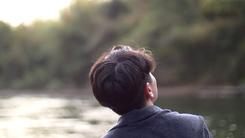 young guy try to reach out for the sky sitting by the river.mov