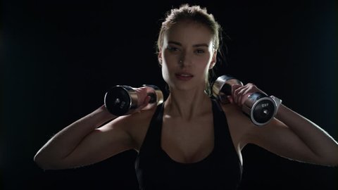 Fitness woman training dumbbell exercise on black background. Sport model workout with dumbbells in gym. Fit girl lifting dumbbell in slow motion. Yound woman training body