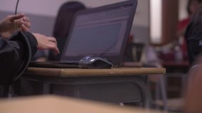Arms of a young woman in classroom using a laptop to take notes and arrange files