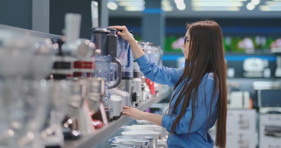Young beautiful sexy brunette chooses a blender for the kitchen in the appliances store | Shutterstock HD Video #1027360916