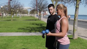 Side view of focused woman training arms with dumbbells. Sporty young girl and instructor doing exercise. Concept of sport