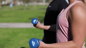 Cropped shot of young people training with dumbbells in park. Closeup view of man and woman during workout. Concept of sport