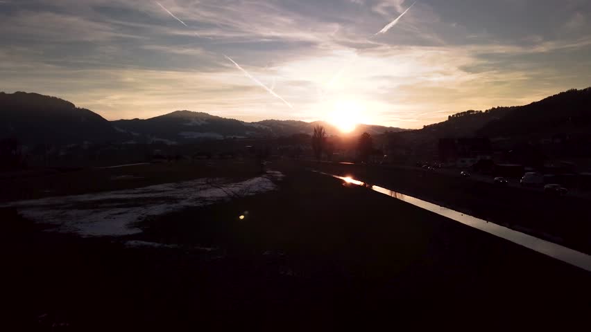 Beautiful moody winter wonderland scenery in Switzerland with a reflective river, cars and a village while sunset.