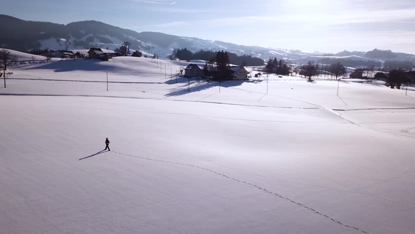 Young man walks through a big snowy field in the winter in Switzerland.