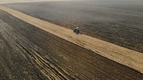 Aerial view of the tractor with the agricultural unit performs the plowing, the cultivation of the soil of brown color in the dry Sunny weather. Bad harvest concept