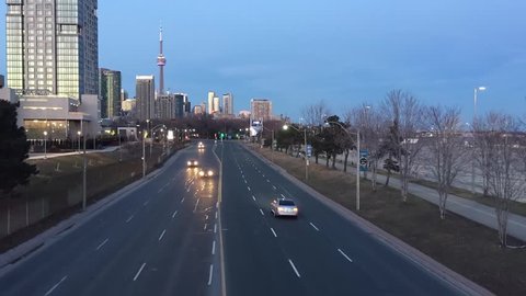 Timelapse video footage of cars driving on a busy road street highway freeway, filmed from a bridge in evening. Aerial view of Gardiner expressway, Toronto city skyline and CN Tower on the horizon.