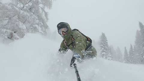 ACTION: A snowboarder rides through deep snow and turns in the fresh powder. Snow splashes into the camera and athlete. Winter sports activities.