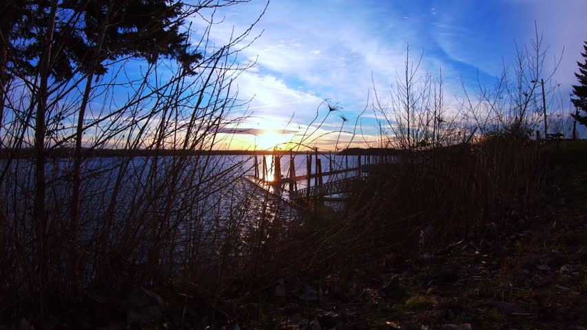 Time Lapse of sunset on the Columbia River with grass, bushes and trees in foreground, beautiful blue sky.