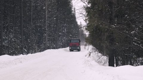A truck carrying ore rides along a narrow winter forest road. Slow motion.