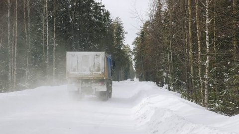 A truck carrying ore rides along a narrow winter forest road. Slow motion.