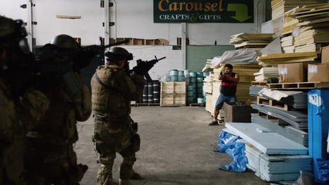 Special ops military SWAT team have shootout with villains in warehouse under dramatic daytime lighting. Daytime medium to closeup shot on 4K RED camera.