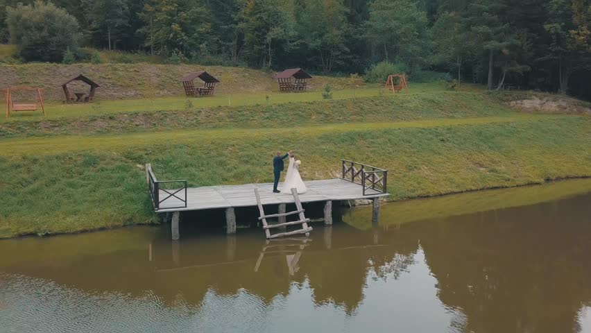 Groom with bride near lake in the park. Wedding couple. Happy family. Man and woman in love. Lovely groom and bride. Making a kiss. Aerial shot