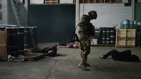 A special ops military SWAT team member emerges from dark smoke filled warehouse walking towards camera taking out bad guys in warehouse under daytime lighting. Daytime wide shot on RED camera