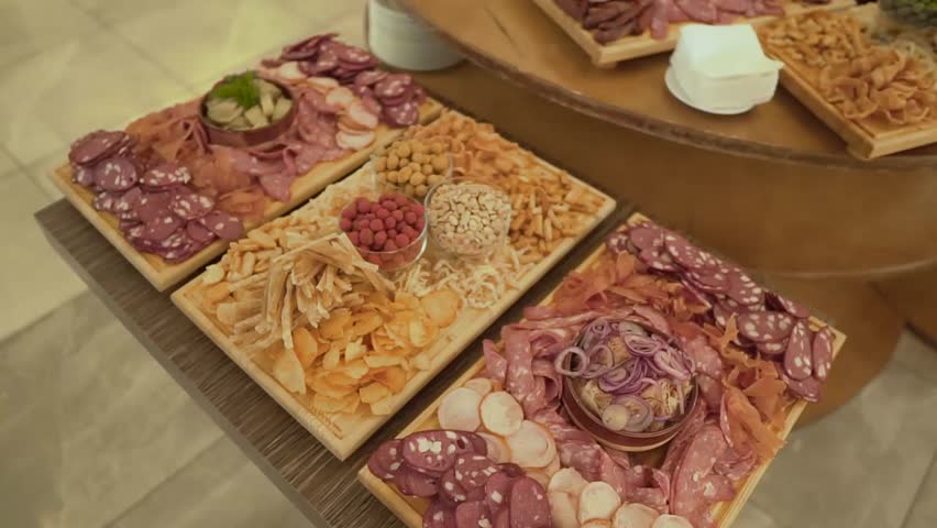 Three wooden boards with salty food as a part of food buffet. there are many kinds of smoked meat and cheese, chips and nuts. The background is blurred.