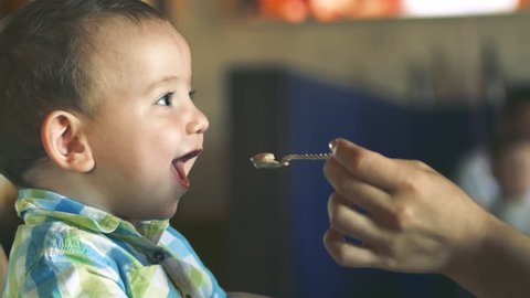 Mother Gives Baby Food from a Baby Spoon in a Restaurant, a Child Eats Willingly. Cute Little Baby Eating Her Dinner. 4k. Child eat porridge.