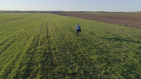 A man/guy dressed in jeans and a shirt with a jacket in his hand runs across the open field to meet a girl in a blue dress on a Sunny spring/summer day, aerial photography, 