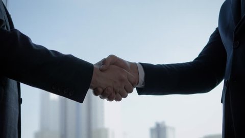 Close up of the hands of top managers in business suits, shake hands with each other, against the window in the office, agree to a deal or say hello. Slow motion, unrecognizable person