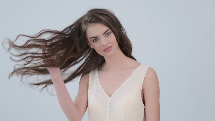 Beautiful woman with long curly brown hair. Fashion model looks to the camera at studio. Closeup face of an attractive brunette woman. Sexy model with a saexy look. 4k footage. Slow motion. 